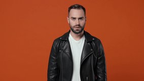 Crazy displeased young bearded man 20s in black leather jacket posing isolated on orange color background studio. People lifestyle concept. Covering ears with fingers screaming keeping eyes closed