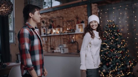 Two young men without a boy filmed at a slow speed, jump up and shake hands next to the tree decorated with lights. Bright living room decorated with bright Christmas tree lights. Happy winter