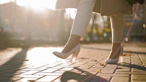Unrecognizable Beautiful Business Woman Legs in high heels walks through city park to work in the office in autumn in sunset light. Close-up. Slow motion. High quality FullHD footage