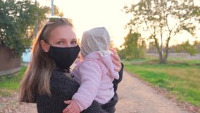 Front view, a young beautiful girl in a medical black mask with a small child in her arms looks at a beautiful sunset. then the girl turns to the camera - Powered by Shutterstock - Get 15% off with code: PIKWIZARD15
