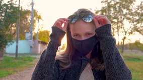 Front view, a young beautiful girl in a medical black mask lifts her glasses on her hair and looks around in the rays of the setting sun. - Powered by Shutterstock - Get 15% off with code: PIKWIZARD15