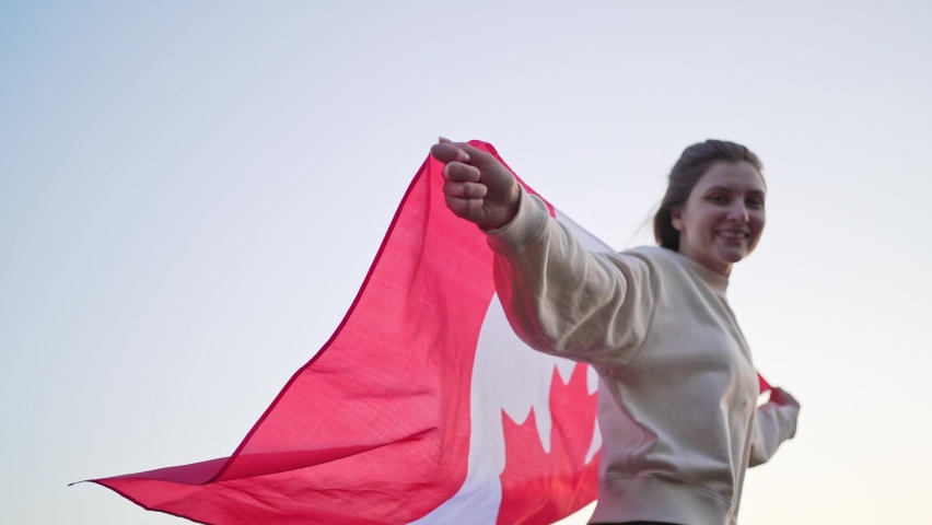 A woman runs with the flag of Canada against a clear sky. Patriotism of citizen of Canada Royalty-Free Stock Footage #1062356662
