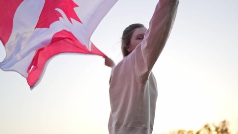 A woman runs with the flag of Canada against a clear sky. Patriotism of citizen of Canada