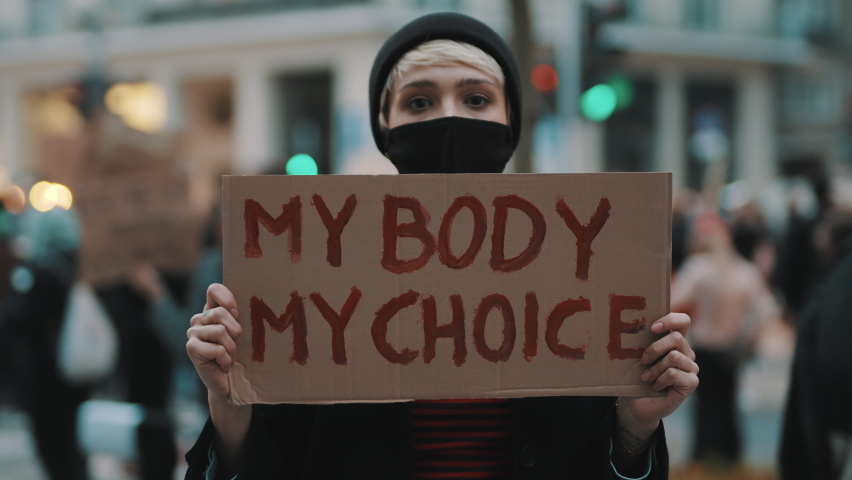 Woman holding a sign My Body, My Choice. Protest against tightening of the abortion law . Nationwide women's strike. Wearing protective face mask against COVID-19 Coronavirus. High quality 4k footage Royalty-Free Stock Footage #1062357241
