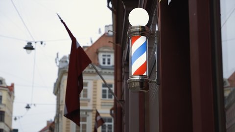 Bright red white blue barbershop pole on wall with LV flag in background