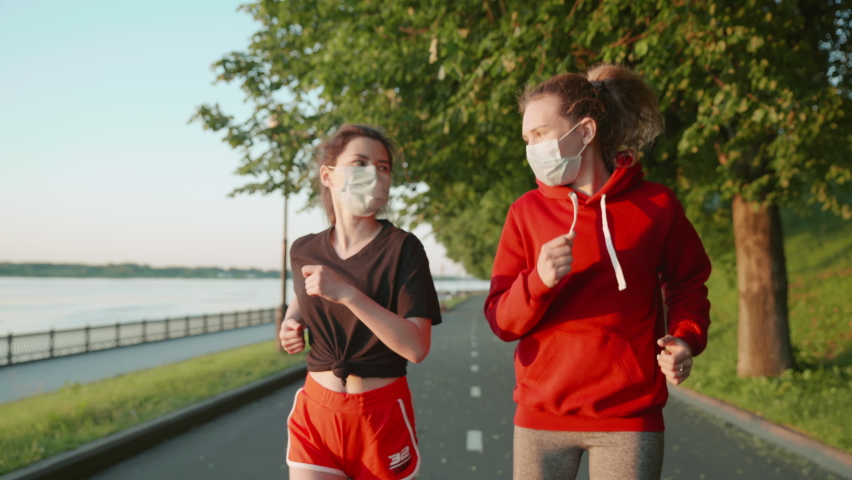 Brunette and blonde run in Covid. New life after quarantine. Girls keep a social distance and run along the embankment in protective masks. Concept of healthy lifestyle, training, jogging. Royalty-Free Stock Footage #1062360049