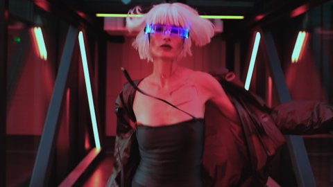 A woman in shining glasses runs down the corridor with neon. High quality FullHD footage