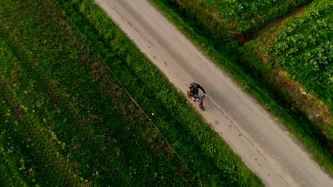 Aerial view of man with helmet that rides his electric bicycle alone on a countryside street, during a sunny day