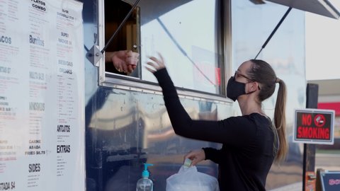 This video shows a young caucasian woman customer wearing a protective face covering mask and receiving extra sauce from an outdoor food truck.