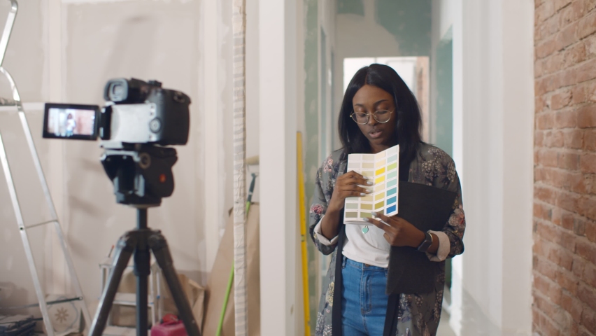 African woman designer choosing paint color for house and recording video for blog. Afro-american decorator blogger filming video on camera having internet blog about renovation Royalty-Free Stock Footage #1062362611