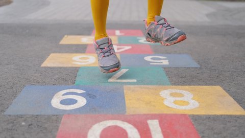Legs of little girl in bright tights jumping over numbers on asphalt