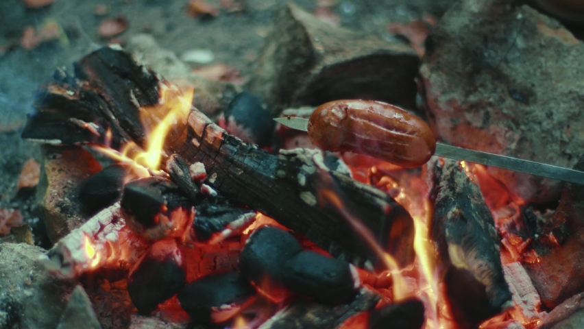 Close up hands frying sausages over a fire in forest. Campfire on autumn evening in the woods. Friendship happiness cook fireplace. Close up. Slow motion