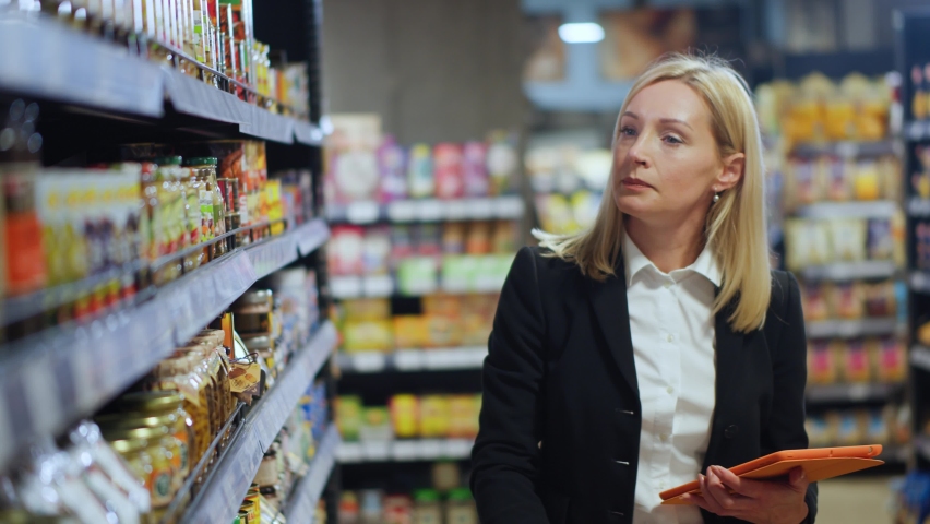 Busy focused caucasian woman in formal wear finding foods in grocery store checking shopping list on tablet. Organic market. Casual lifestyle. After work. Royalty-Free Stock Footage #1062365188
