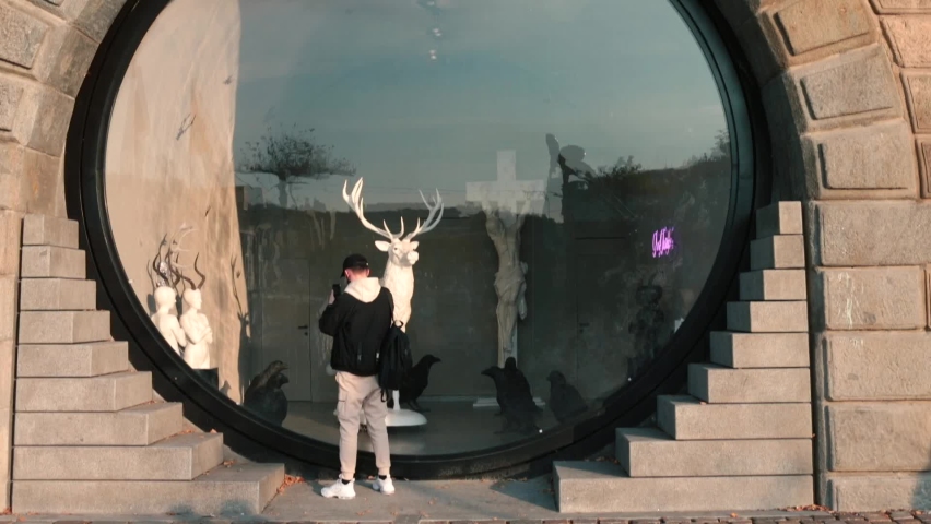 Modern architectural design solution. Young man takes photographs in front of large modern round shop window in city. Passers-by pass by quickly. 