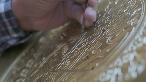 Bukhara master engraves patterns on a tray. Close up, slow motion