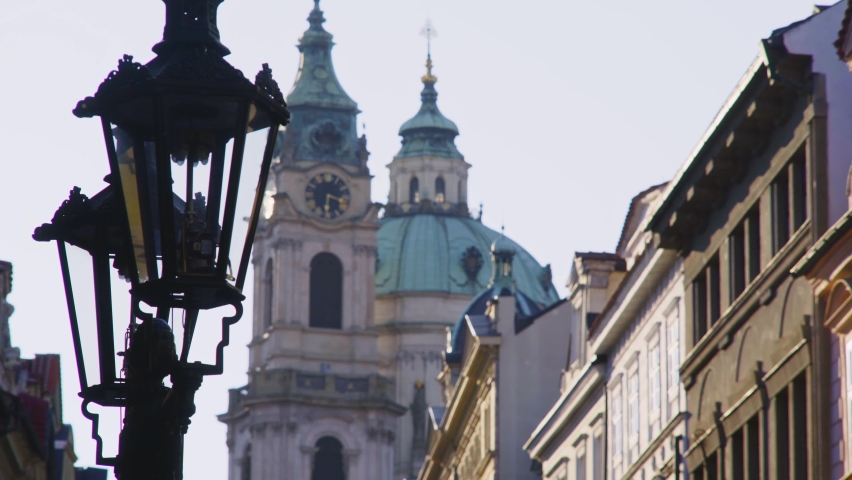 View bell tower Church of Saint Nicholas on Mostecka Street through vintage gas lantern on foreground, old town with historical buildings, Prague, Czech Republic