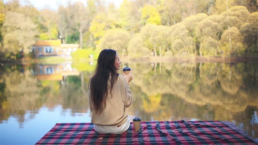Beautiful woman in autumn park with coffee to go on the lake
