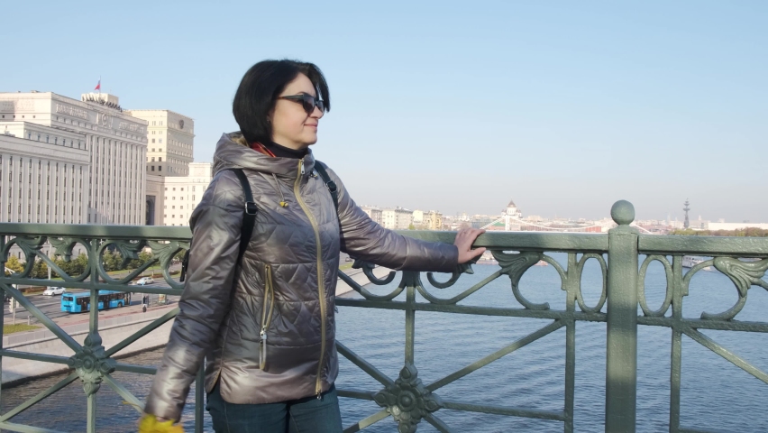 A middle-aged woman, brunette Caucasian race, in a brown jacket with short hair, with a bouquet of yellow leaves, walks on the observation deck a motor ship with tourists is sailing along the river.