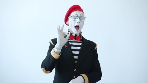 Portrait of happy male mime showing okay and thumbs-up hand gestures and winking expressing recommendation on white background. People and approval concept.