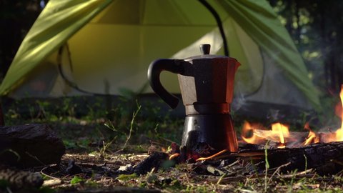 Coffee maker near a fire. Green tent in the background. Travel concept