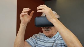 Amazed senior grandfather in virtual headset glasses watching amazing 3D video in 360 vr helmet at home. Future technology. Man in VR goggles playing games, looking around, shows emotion of surprise