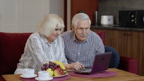 Happy senior elderly couple grandfather and grandmother looking on digital laptop making online shopping and celebrating. Mature old husband and wife watching news videos, using social media at home
