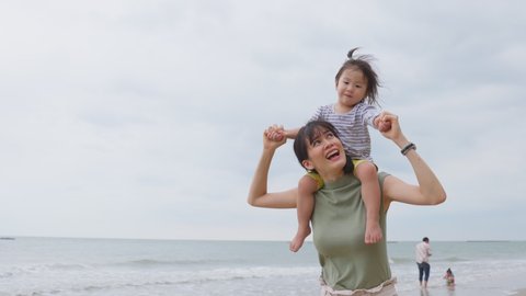 Asian family on vacation. Beautiful mother carrying little baby girl on shoulder walking on the beach together with happy and smile. Soft touch, love care, protection of mom and child relationship.