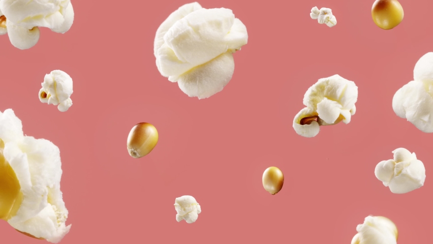 Lots of corn kernels popping one by one on coral pink background while camera is slowly moving into the frame center. Popcorn hanging in the air. Snack making  | Shutterstock HD Video #1062386086