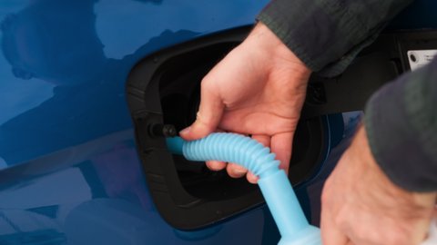 Close up man filling a diesel engine or exhaust fluid DEF from canister into the tank of blue car.