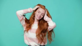 Beautiful cheerful ginger redhead young girl wearing white pink sweater posing isolated on blue turquoise color background in studio. People lifestyle concept. Dancing shaking head with flowing hair - Powered by Shutterstock - Get 15% off with code: PIKWIZARD15