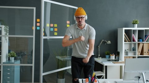 Crazy young man hipster is enjoying music through headphones dancing and having fun in office alone. Workplace and relaxation activities concept.