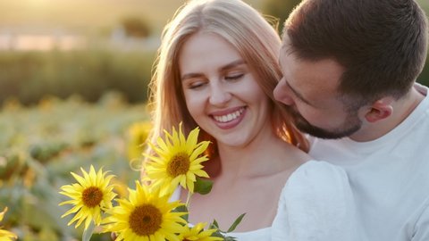 Beautiful happy couple hugging and kissing on the sunflower field. girl with her boyfriend resting outdoors. Sunset.