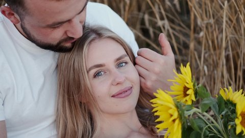 Couple relationship goal concept. woman and man laying in a countryside field of wheat. The woman is holding a bunch of sunflowers.