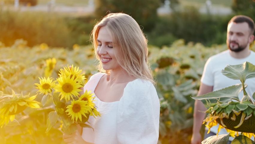 Beautiful happy couple hugging on the sunflower field. Blond girl with her boyfriend resting outdoors. Sunset.