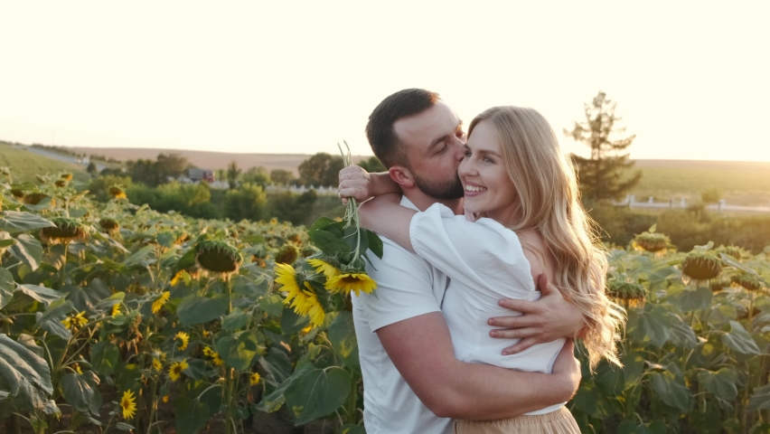 Beautiful happy couple hugging on the sunflower field. Blond girl with her boyfriend resting outdoors. Sunset.