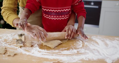 Close up of African American female hands with little cute child at table in home kitchen making dough for cookies. Small kid helping mom to bake xmas biscuits. Holiday preparations concept