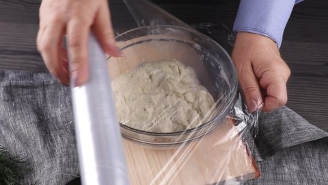female chef covering by plastic wrap or cling film fresh yeast dough