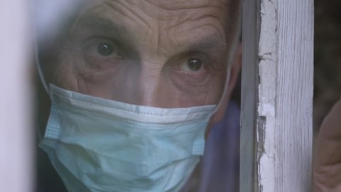 demented old man wearing medical face mask staying behind window glass of nursing house coronavirus concept.