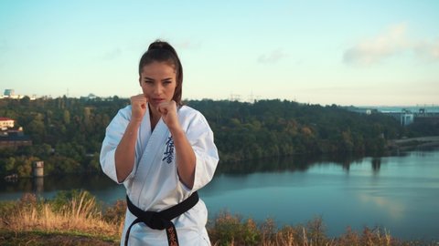 A young beautiful girl, with long hair pulled up ponytail, kimano, karate, conducts series punches and kicks. Dynamic shooting handheld, with natural shaking against the background nature, rivers