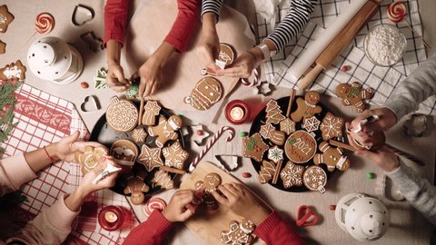 Family is decorating a traditional gingerbread. Xmas flat lay video. Christmas and New Year holidays mood. Group of people glaze a cookie. Top view of home table