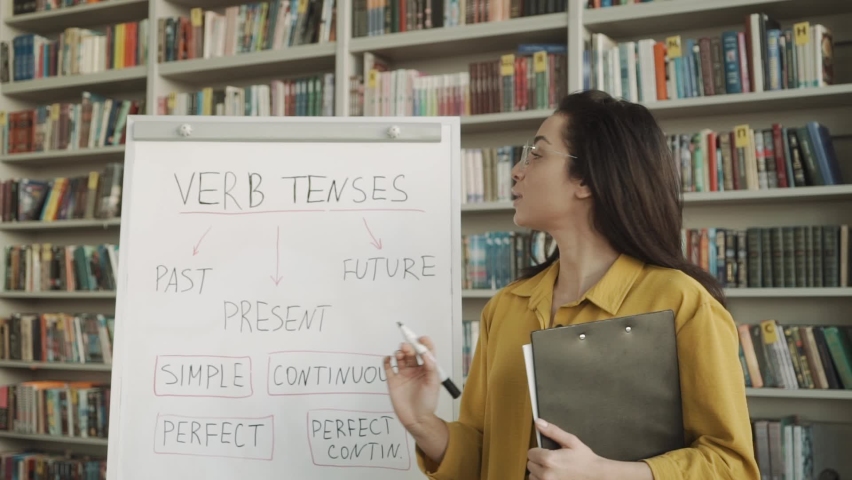 Young female english language teacher standing in front of the whiteboard and studying in classroom Royalty-Free Stock Footage #1062406489