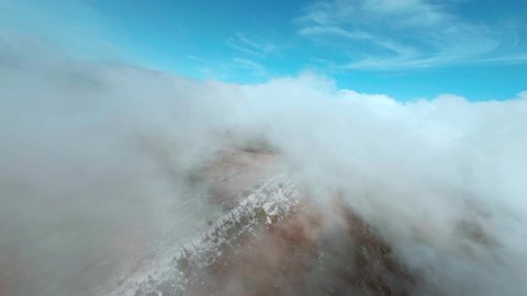Fpv sport drone taking off over hills through misty haze to blue sky. Aerial cinematic shooting mountain terrain through white clouds. Misty haze over highlands from bird above.