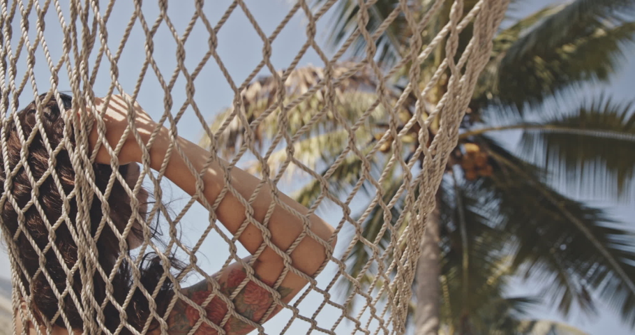 Asian girl on hammock by tropical beach next to the palm tree watching something. Exotic, relax, lifestyle, advertising, commercial concept. Close shot on Canon camera with 12 bit color depth.
