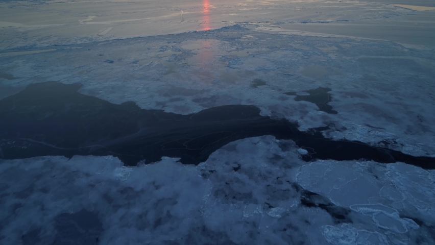 From great height unique frozen open ocean, sea cracked ice on surface. Cinematic orange sunset sun. Epic nature of planet. Winter cold season. Open space horizon. Shipping, navigation. North. Aerial Royalty-Free Stock Footage #1062411418