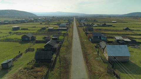 Aerial Russia traditional old wooden houses poor village, country dirty road streight. Baikal region life of ordinary people. Distinctive rustic Buryatia backyards. Drive car on onto deserted road. 4k