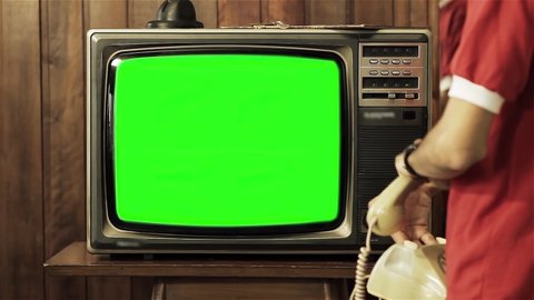 Young Man holding Old Telephone and Watching Retro TV with Green Screen. 4K Resolution.