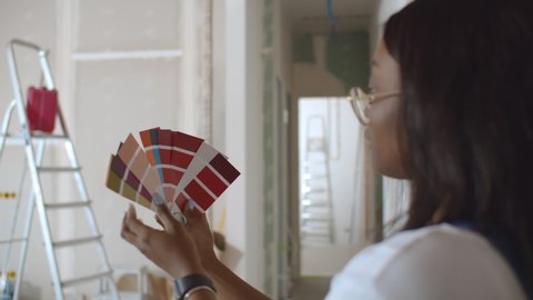 Young african woman choosing paint color from swatch for new interior design. Afro female holding palette with colors choosing paint for wall decoration