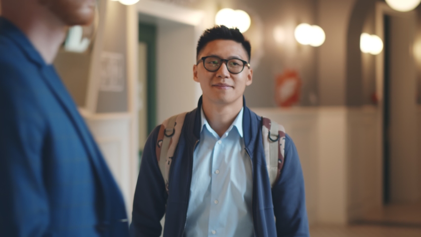 Portrait of smiling asian male student walking on corridor after classes. Positive young japanese college guy in glasses with backpack walking on university building hallway Royalty-Free Stock Footage #1062412630