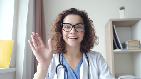 Attractive young female doctor wear eyeglasses make online video call consult patient on laptop. Medical assistant therapist videoconferencing. Web camera view. Telemedicine pandemic concept. 