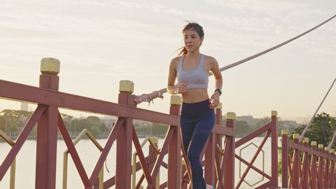 Asian young beautiful woman running for health in the evening sunset on the bridge in public park. The athlete fit and firm girl exercising by jogging workout sport outdoor for her healthy wellness.